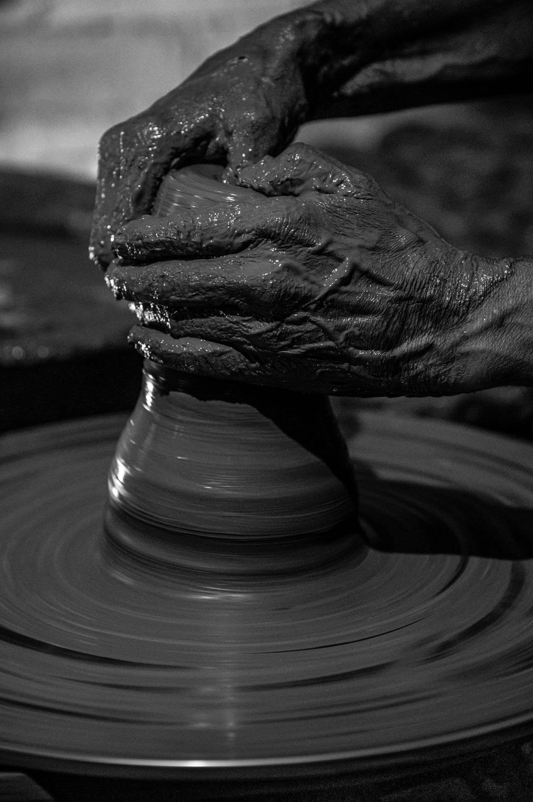 A black-and-white close-up of a potter's hands shaping a vessel on a spinning wheel