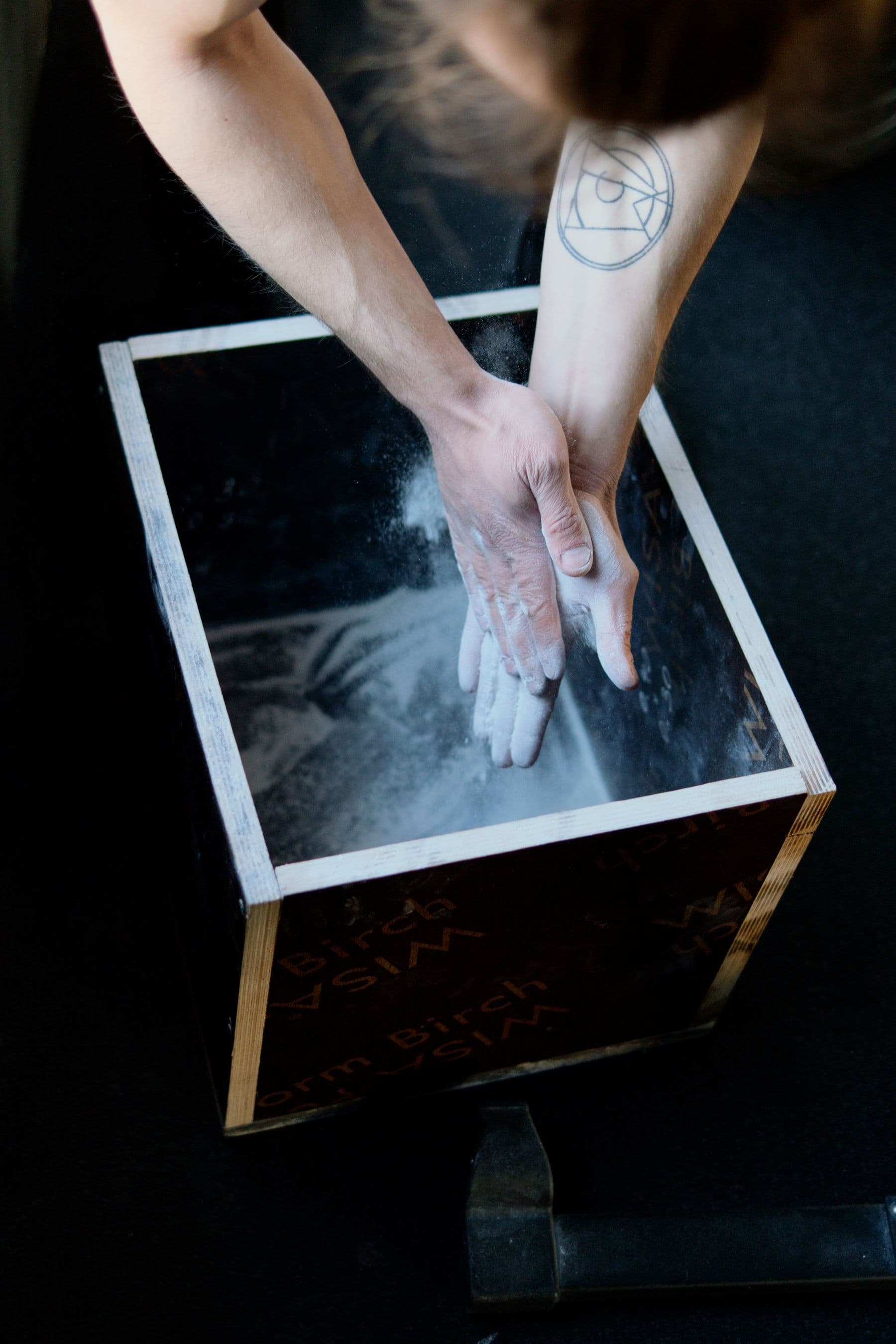 An athlete clapping chalk-covered hands over a wooden chalk box