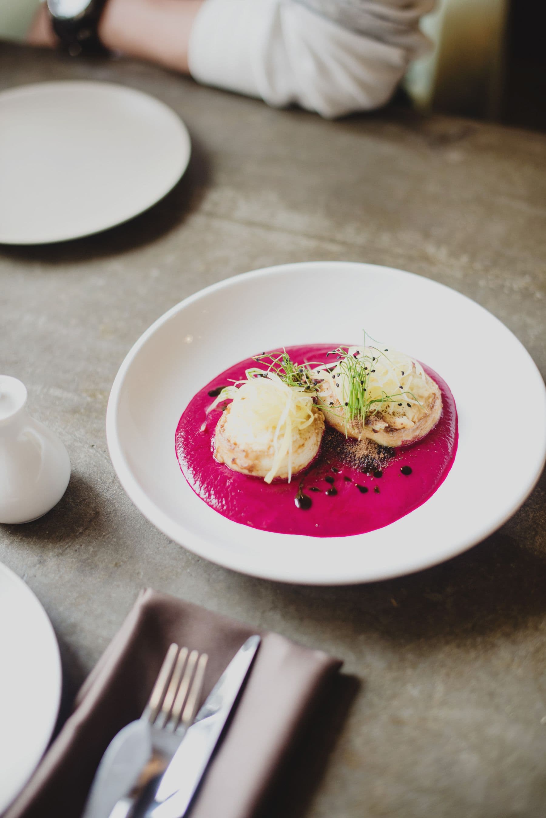 A plated dish with a vivid beet purée and fresh garnish on a white plate