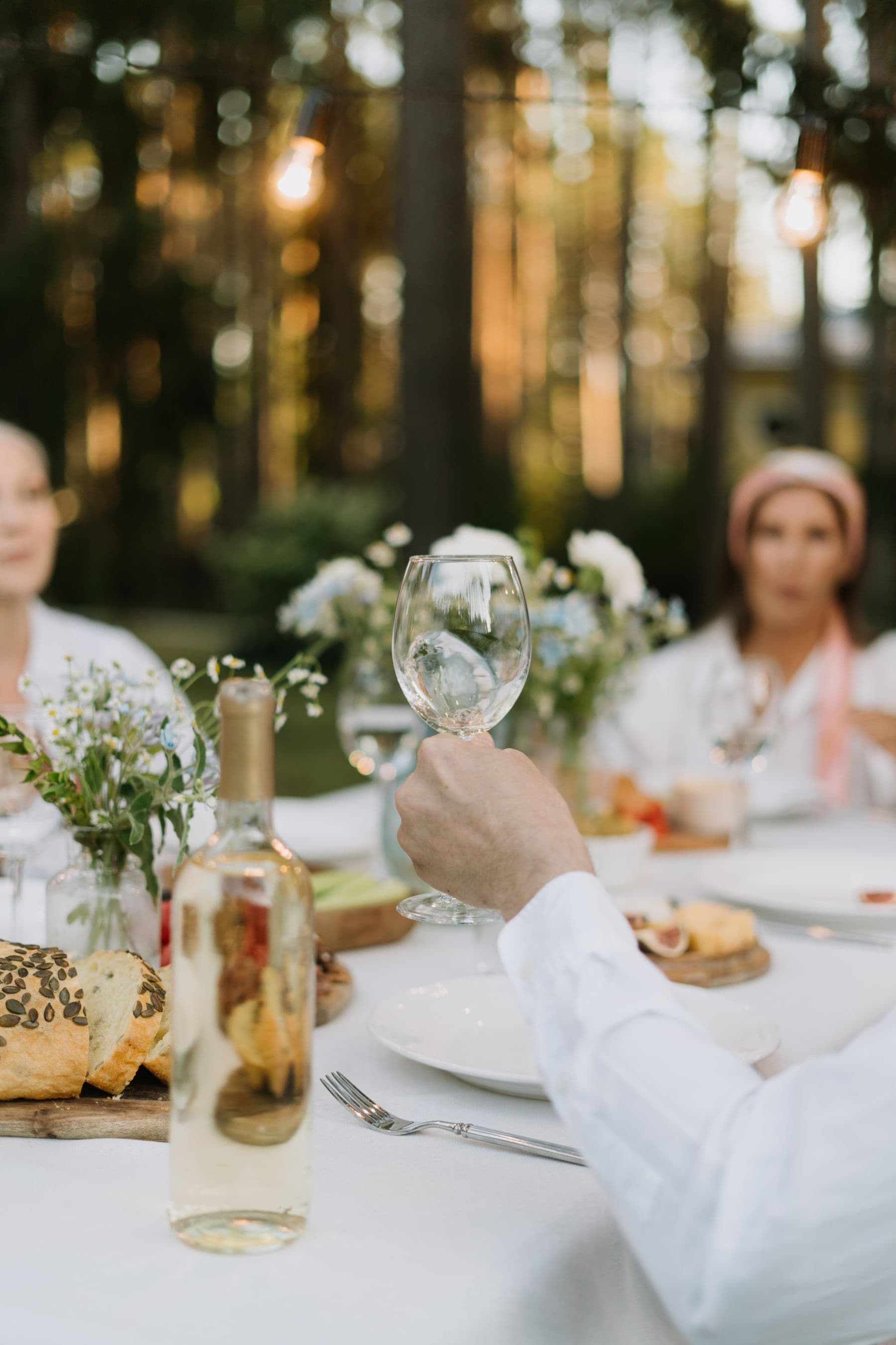 A guest raising a wine glass at a garden dinner table in golden evening light